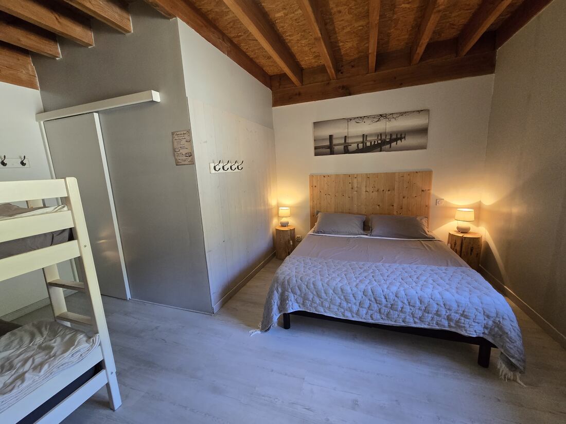 Habitación con cama de matrimonio y litera bajo la viguería