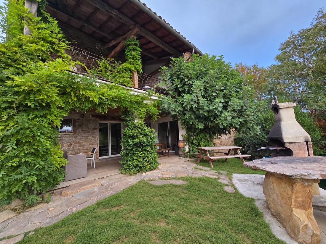 El jardín delante de la casa, la barbacoa de piedra y la mesa bajo la glicina